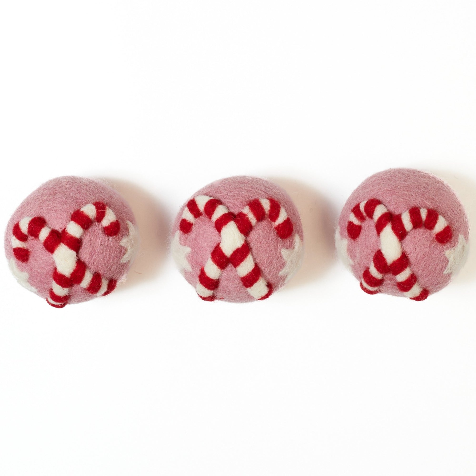 Three pink and white candy cane patterned dryer balls on a white background