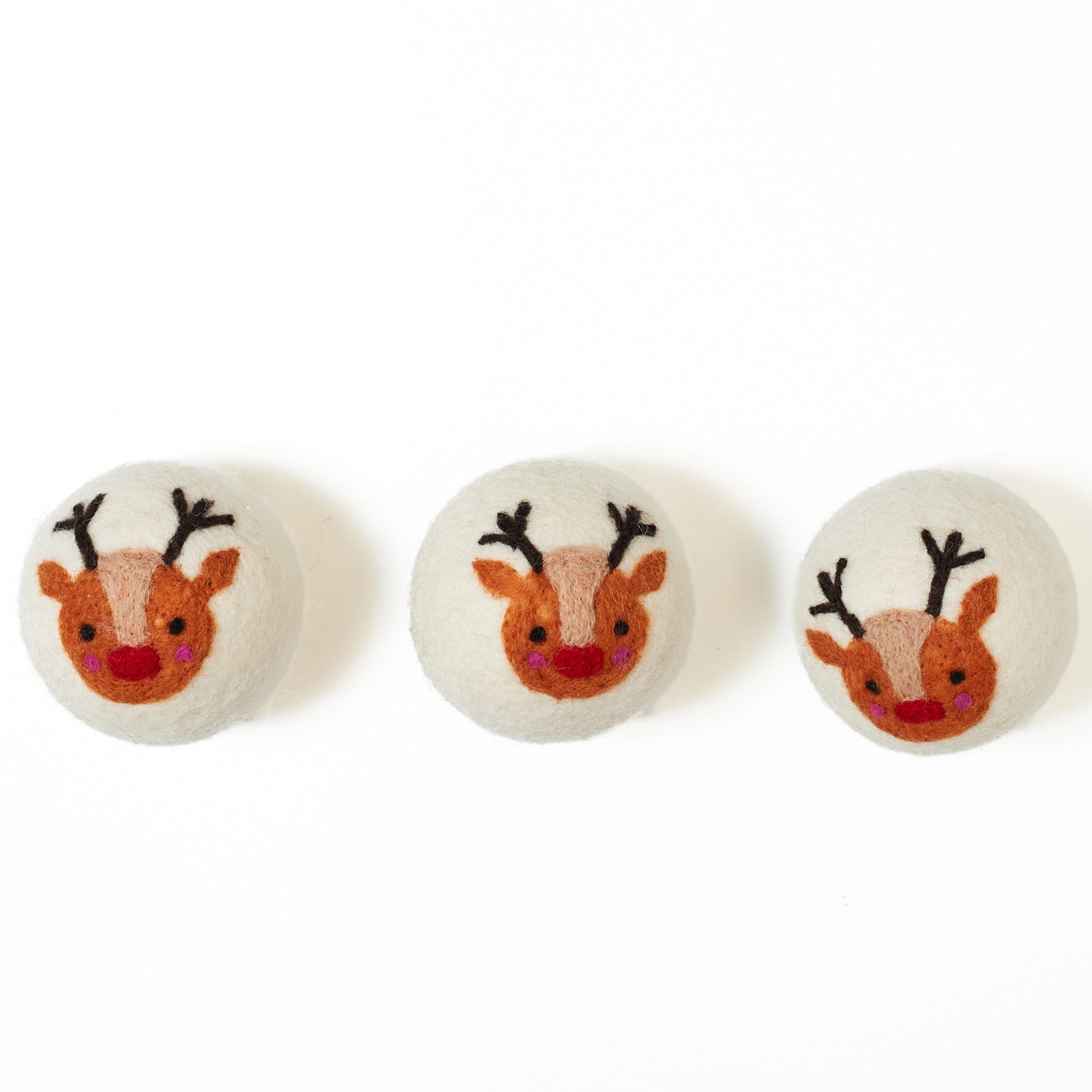 Three dryer balls with reindeer faces on a white background